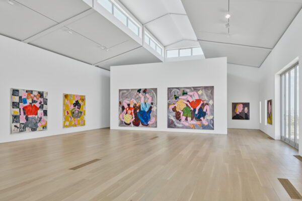 A large, white, wood floored gallery space contains large-scale paintings of figures.