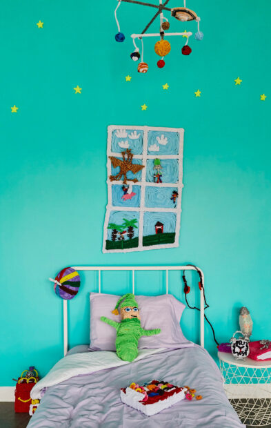 A sculpture of a child's bedroom, with a solar system mobile and a window.