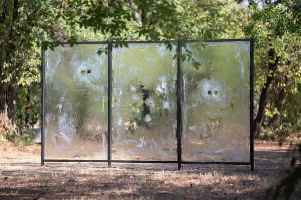 Sculpture of three panels of glass that has foggy areas with eyeholes burned out