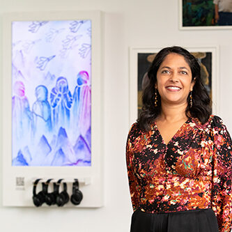 A photograph of artist Sneha Bhavsar standing in front of her work.