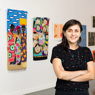A photograph of artist Nela Garzón standing in front of her work.