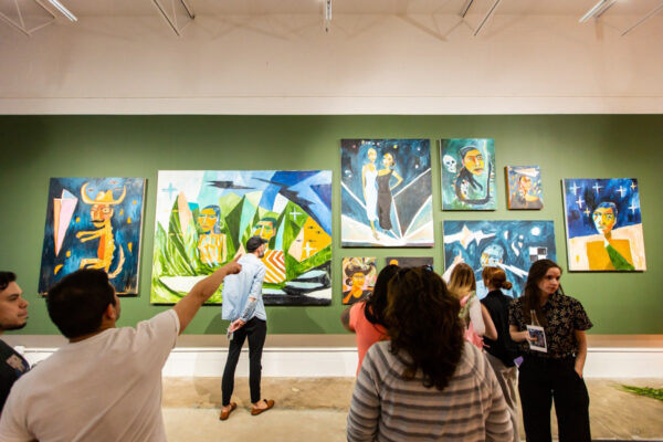 Image of visitors looking at figurative paintings on a green wall