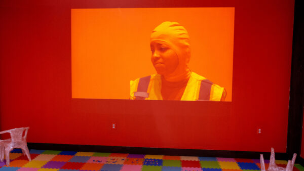An installation by Hiba Ali featuring a projection on a red wall of a figure looking off into the distance.