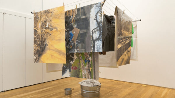 An installation image of a work by Maria Cristina Jadick featuring a clothes hanging rack with photographs printed on fabric hanging like laundry.