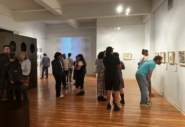 Image of visitors in a gallery space looking at objects on a wall