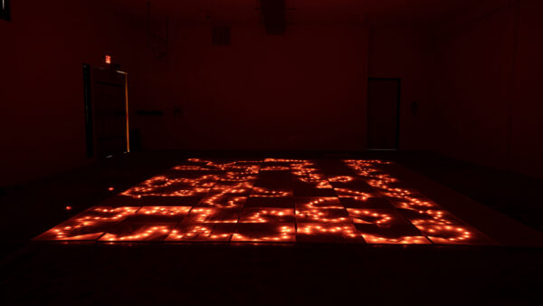 An image of an installation by Ranran Fan featuring a lighted artwork on the ground in a darkened room.