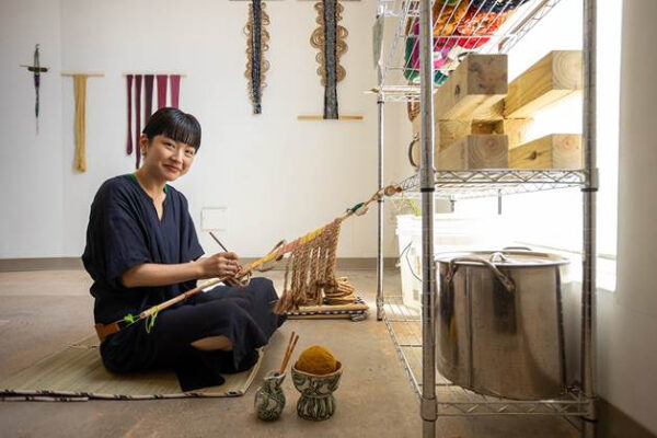 Photo of an artist using a back strap loom in her studio