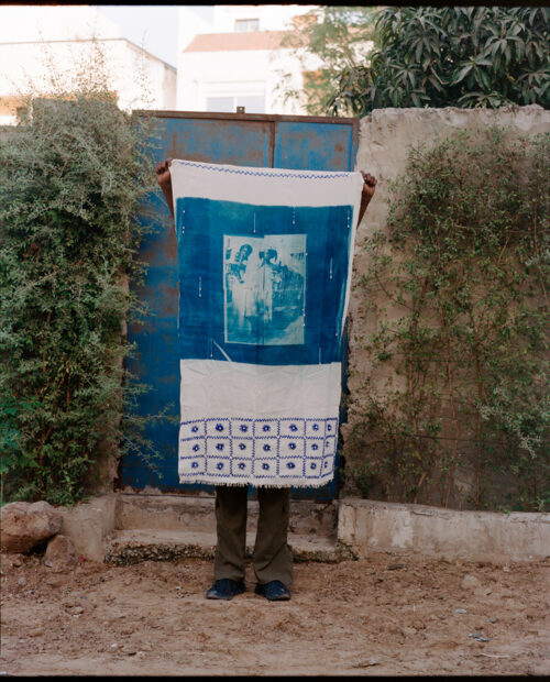 A photograph of a person holding a large alternative process print on fabric in front of their body.