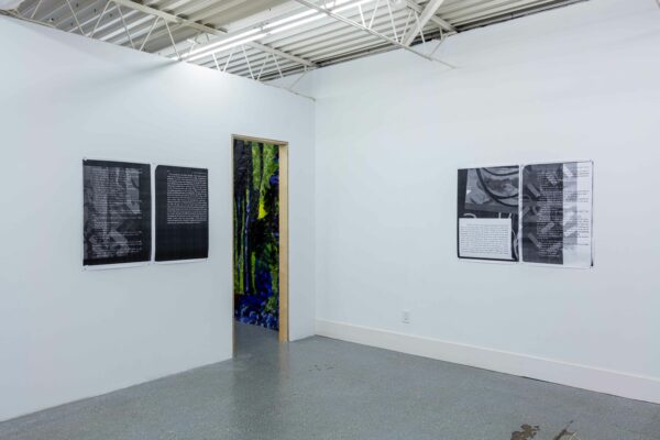 Installation view of posters on a wall and a view of large painting on a tarp