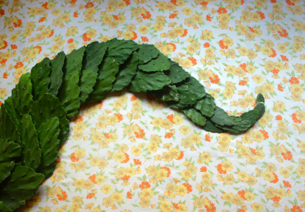 A sculpture made of green leaves on top of a floral print background. The sculpture is in the shape of a tentacle going across the image.