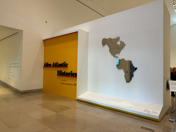 An installation image of a large mirrored work by Hank Willis Thomas featuring the continents of North America and Africa.
