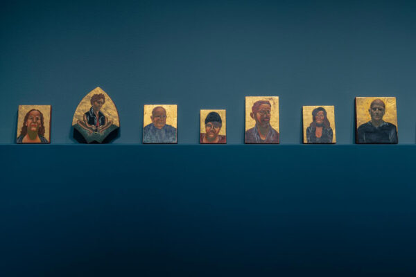 Installation view of portraits with gold leaf against a blue background