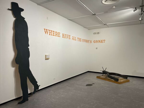 Installation view of an exhibition with a cutout cowboy a large spur, and vinyl text