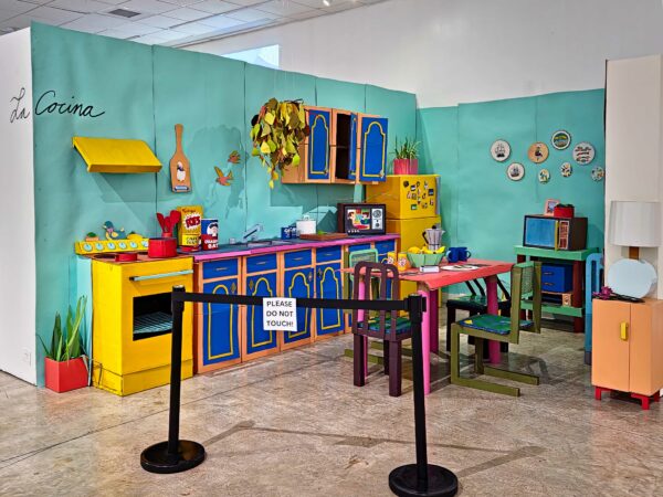 Installation view of a recreation of a colorful kitchen made of cardboard