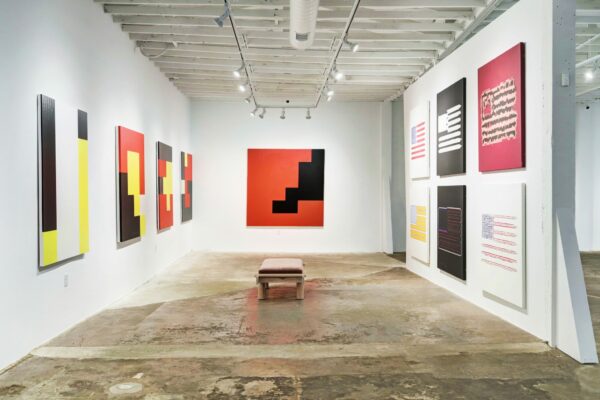 An installation image of an array of abstract paintings hanging in a white-walled gallery.
