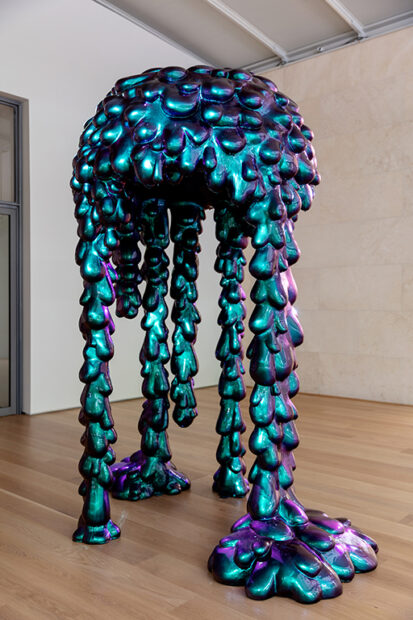 A Sculpture of cascading iridescent drips stands in a gallery