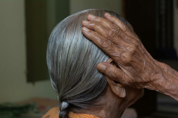 Photo of an elderly woman applying oil to her hair