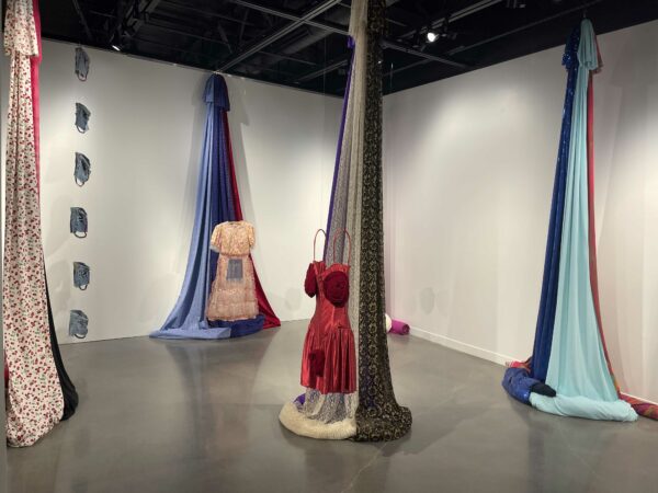 Installation view of draping fabric from floor to ceiling with womens dresses floating in front