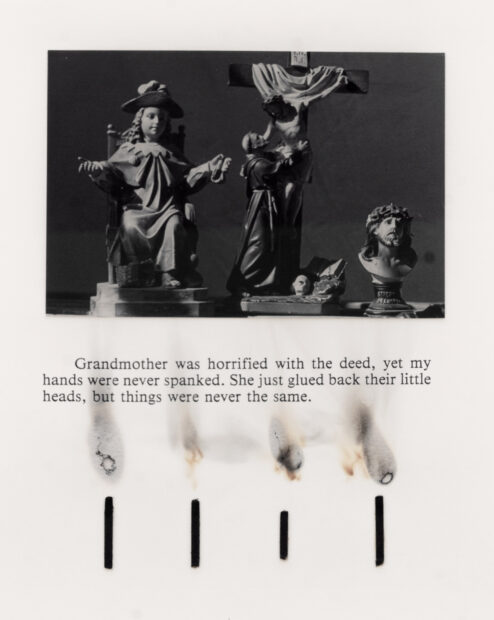 Photo of a black and white photo of a cross, saints, text at the bottom, and a row of burnt matches