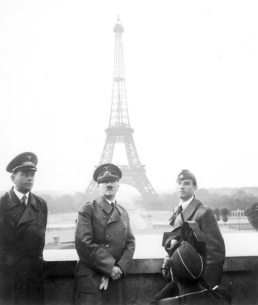 Image of three men at the Eiffel tower including Adolf Hitler