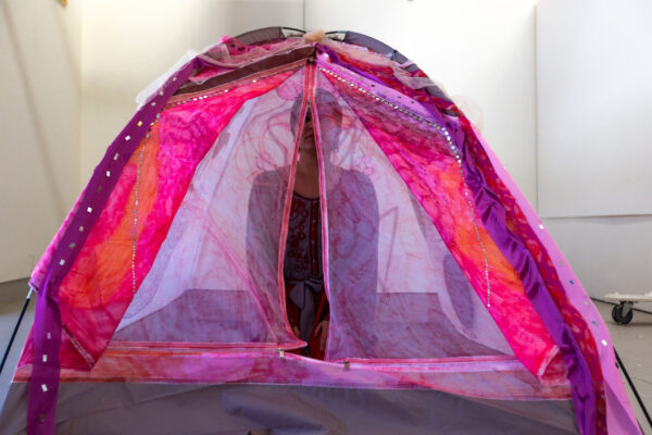 Photo of the artist sitting in a pink and purple tent