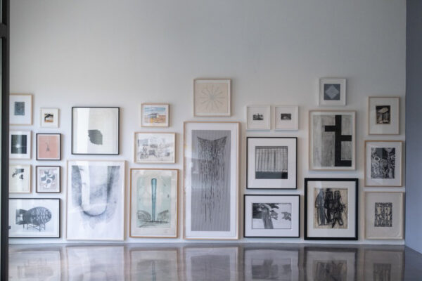 Artworks, many of which are on paper and framed, and in black and white, hang salon-style on a white wall.
