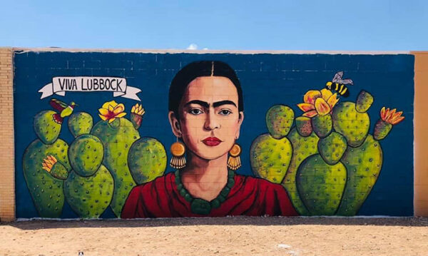 A photograph of a mural on the exterior of a gallery featuring Frida Kahlo set against cacti with a banner that reads, "Viva Lubbock."