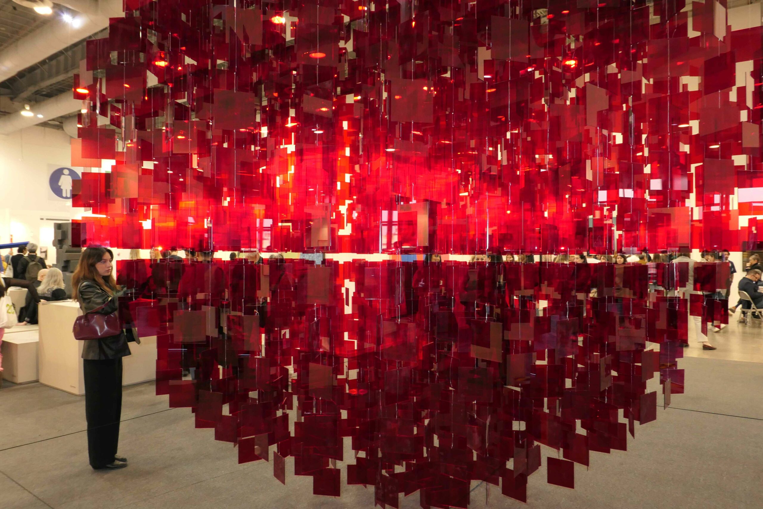 A sculpture comprising hang red plastic pieces with a single viewer standing to its left.