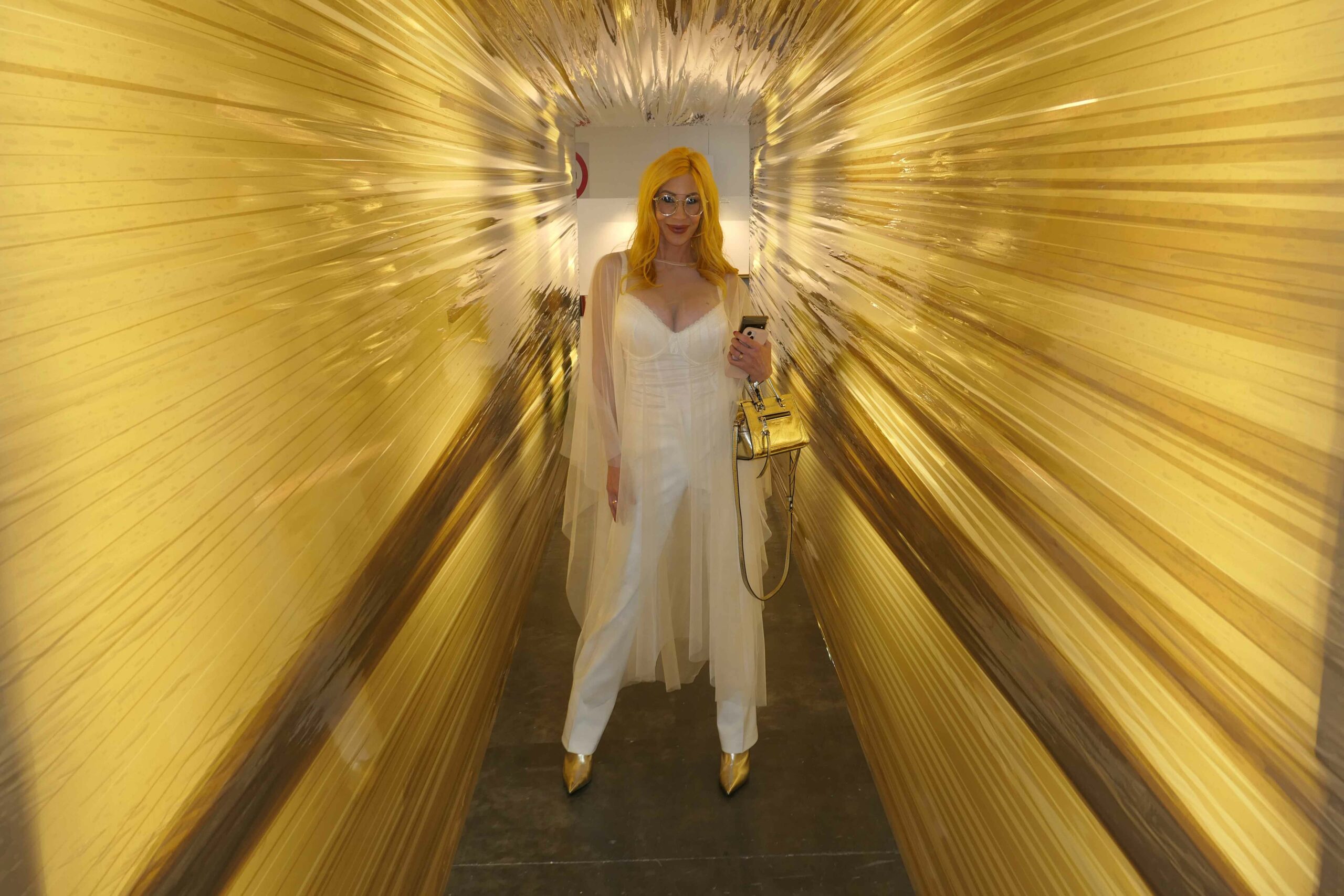 A blonde woman smiles at the camera while standing inside a golden sculpture
