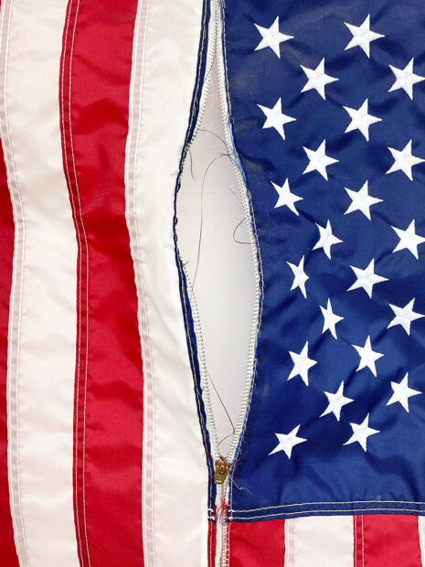 A detail photograph of a work of art made from a U.S. flag with a zipper separating the blue field from the red and white stripes.