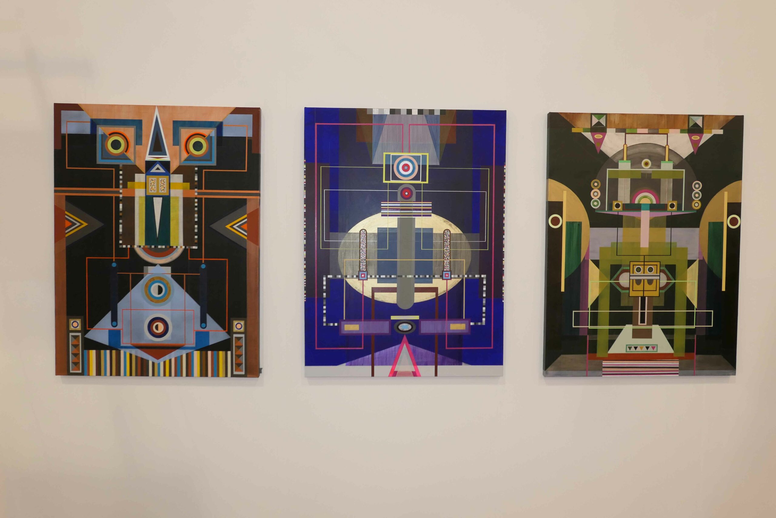 Three paintings in the style of geometrical abstraction hang side by side. 