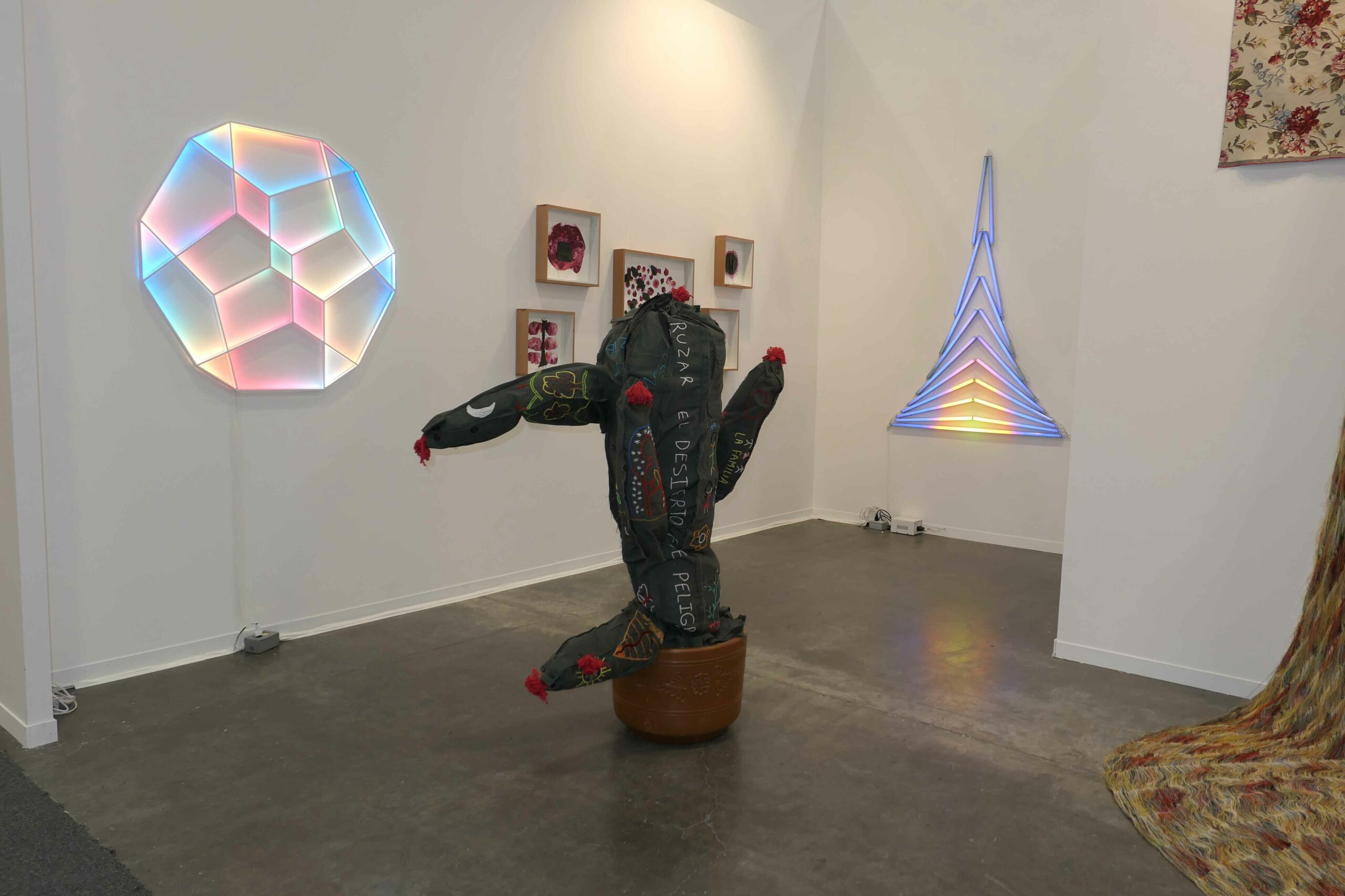 LED light sculptures and a cactus sculpture made from border patrol uniforms fill a booth at an art fair.