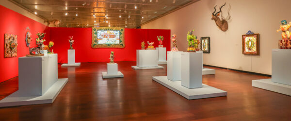 installation view of sculptures on white pedestals, work hanging on white walls and red walls in the background