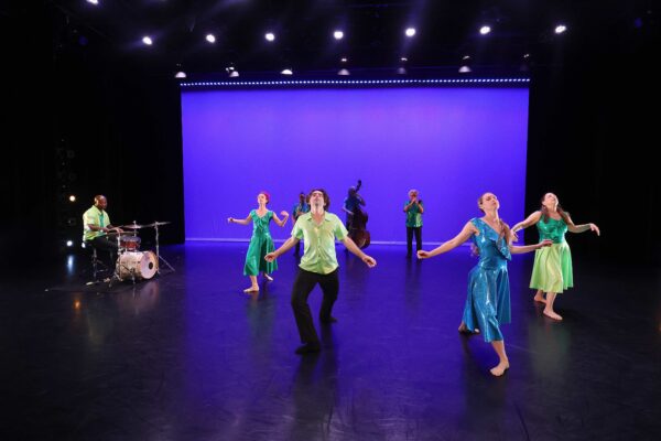 Photo of dancers and musicians performing on stage against a blue backdrop