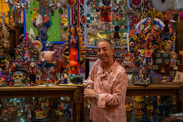 A photograph of gallerist Hank Lee standing in front of an array of art objects from Latin America.
