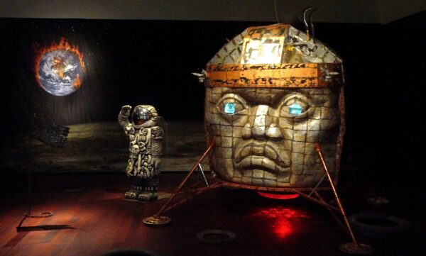 installation of a replica of an olmec head sculture, an astronaut, a fiery earth and discarded tires