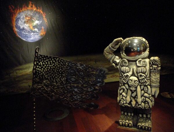 installation view of a sculpture of a cuatlique astronaut with a backdrop of planet earth on fire