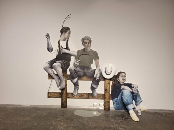 Photo of a work with three people sitting against aa wood fence