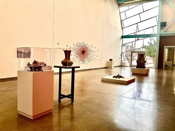 A large art gallery with ceramic sculptures on pedestals, plinths, and installed on the wall.