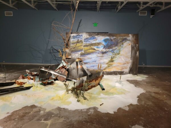 Installation view of soft sculpture, paintings, and tree branches on a gallery floor