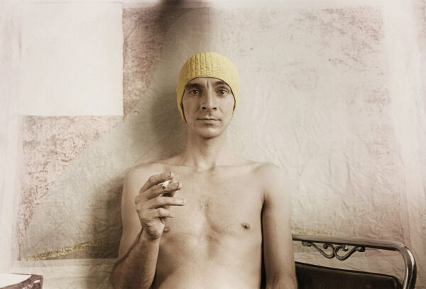 Portrait of a topless man wearing a yellow beanie holding a cigarette