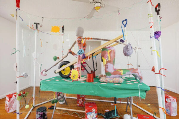Installation of while poles, pipe cleaners, netting, and a green table with objects piled on top