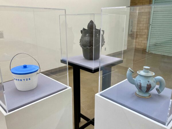 Three ceramic vessels displayed on pedestals with clear coverings protecting them.