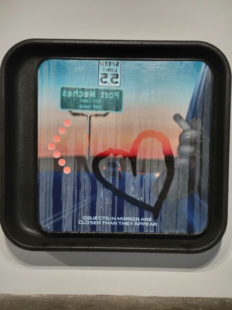 Image of a work replicated a car rear view mirror with a road sign reflection and a heart traced in