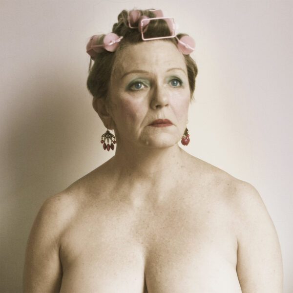 Portrait of a topless woman wearing makeup with pink rollers in her hair