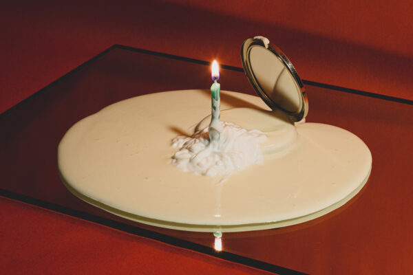 Digital photo of a puddle of creams spilling from a compact with a lit birthday candle