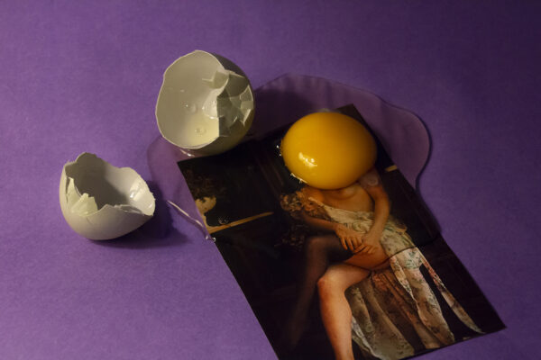 Digital photograph of a woman with an exposed breast with a broken raw egg on top against a purple backdrop