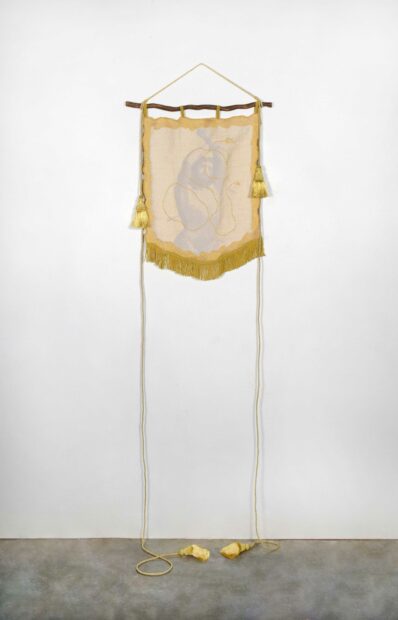 A banner-looking artwork, with long tassels that hang down to the floor, hangs on the wall.