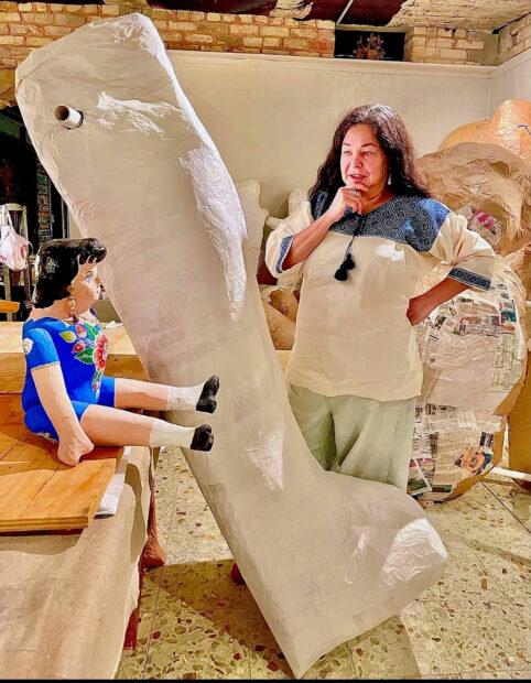 Photo of a woman with her hand on her chin looking at a paper mache doll