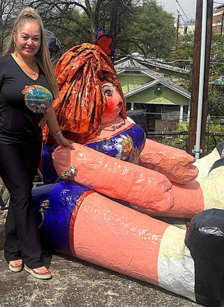 Photo of a woman standing next to a monumental paper mache doll